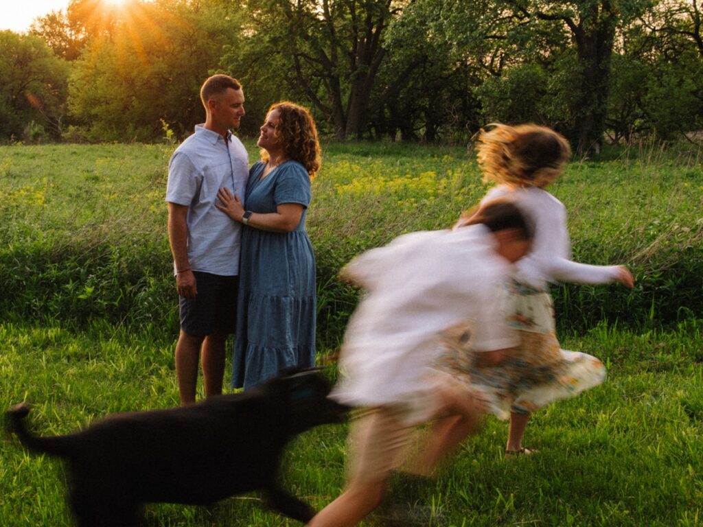 Parents embracing each other as children and dog run by in a blur at family photo session in Elwood, IL. 